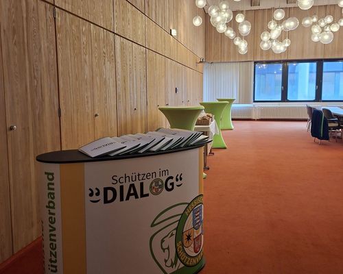 Blick in einen Raum mit einer Theke, auf der Logo des Projekts "Schützen im Dialog" zu sehen ist.