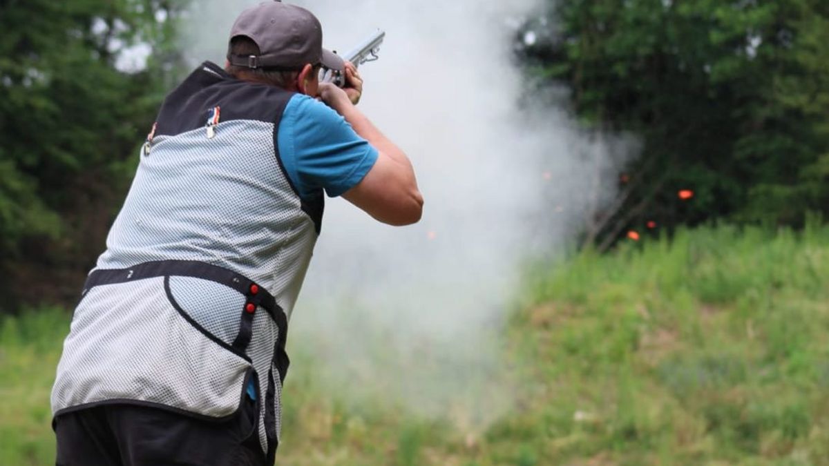 Ein Flintenschütze im Wettkampf. Pulverdampf, im Hintergrund eine zerspringende Wurfscheibe.